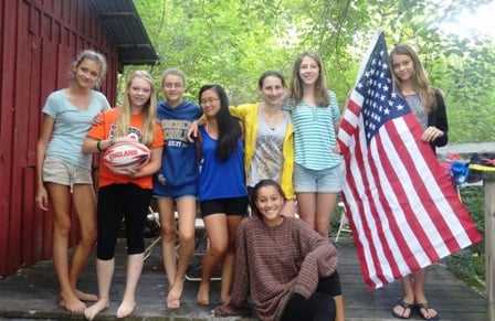 8 female Campers posing with the flag of the United States in a group picture.