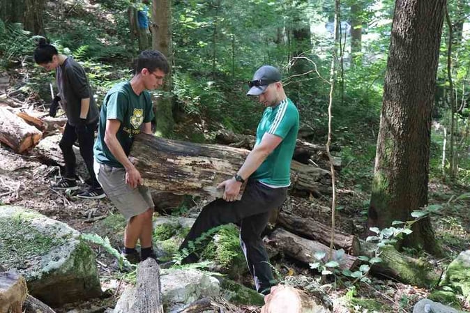 Picture of a staff and a Camper carrying log of wood for the trail