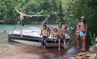 Campers relaxing next to a boat at the river bank after wakeboarding.